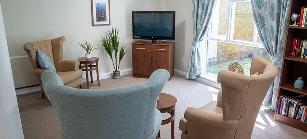 A cosy television corner, home to three grand pastel chairs located around a corner television unit and views into the garden.