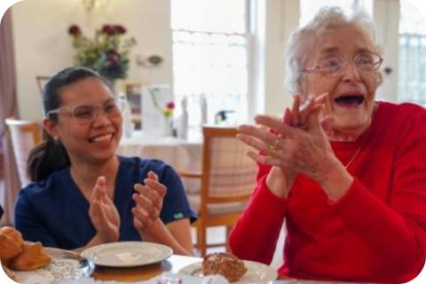 A care worker and resident clapping and smiling