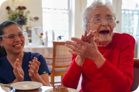 A resident and carer clapping their hands together and smiling as though they are applauding