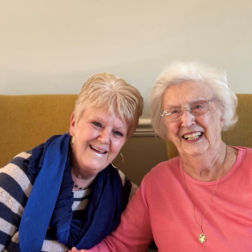 A female resident and her daughter sat next to each other on a sofa and smiling