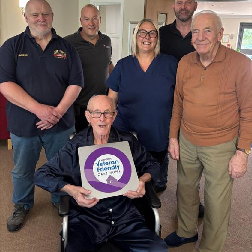 Residents and staff at a Care Home with a resident sat in the front of the frame holding a veteran friendly care home poster