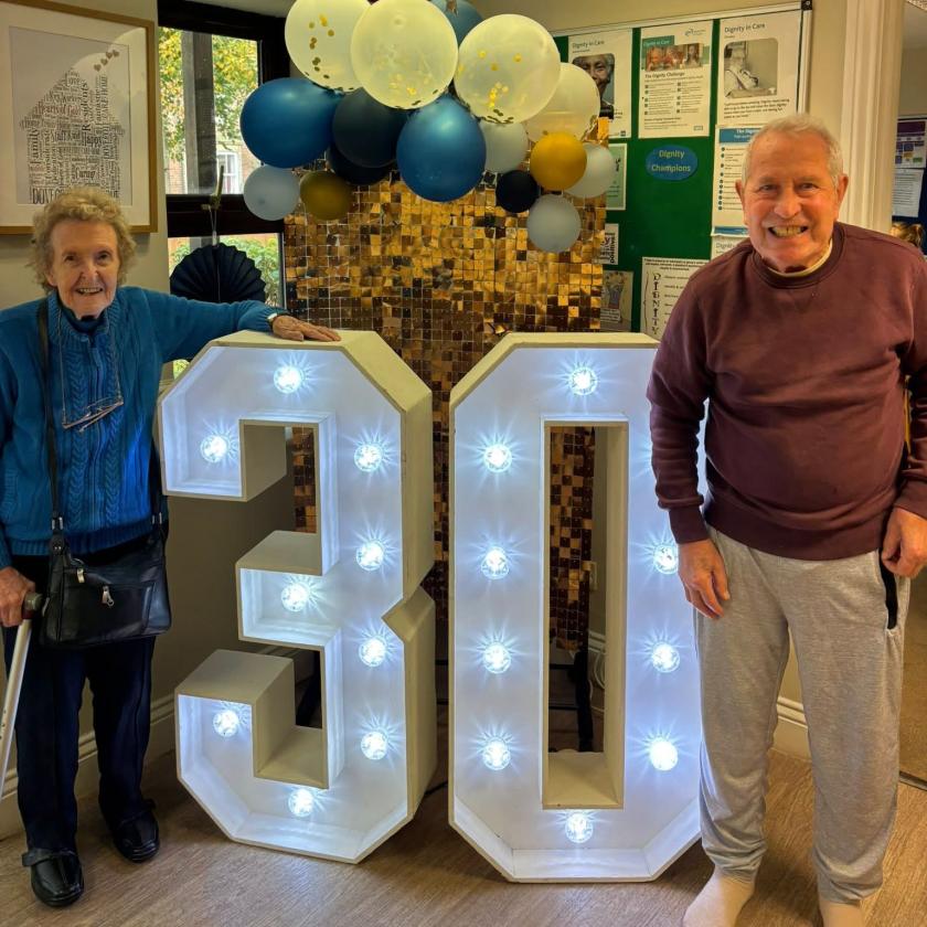 Residents smile for the camera in from of illuminated 30 sign