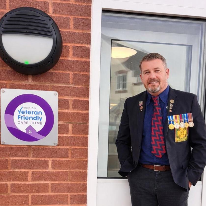 Home Manager stood next to Veteran friendly care home logo