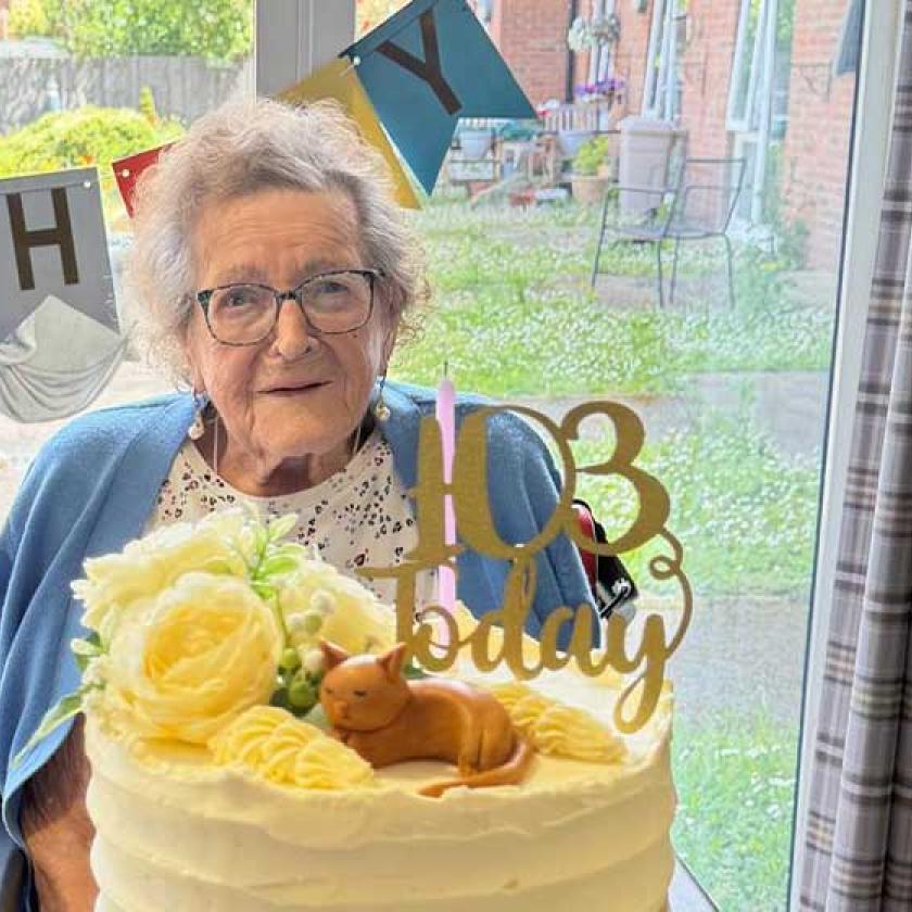 An elderly woman smiles while sitting in front of a birthday cake 