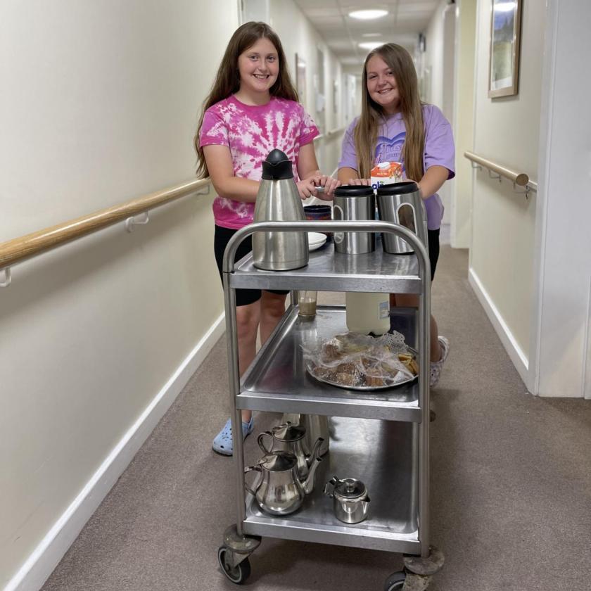 Chloe and Phoebe, the daughters of a carer at Regent pushing a trolley with tea and cakes