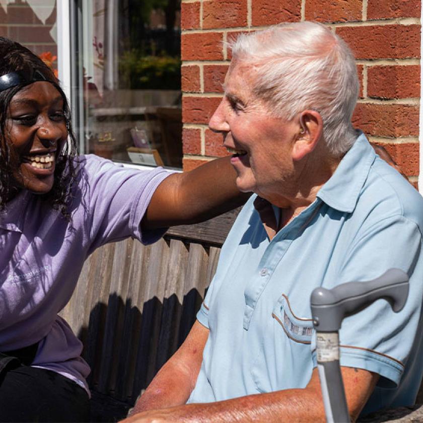 A care assistant puts her arm around a resident while sat outside
