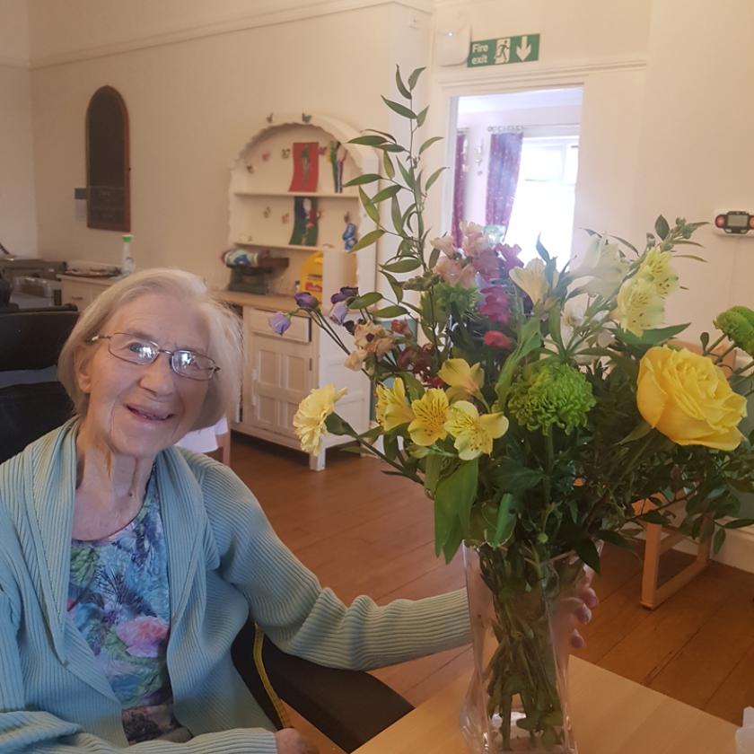 Resident Margery Miles smiling next to a vase of yellow flowers