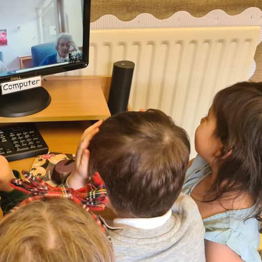 Children gather around a computer to have a zoom call with two residents from Mull Hall Care Home 