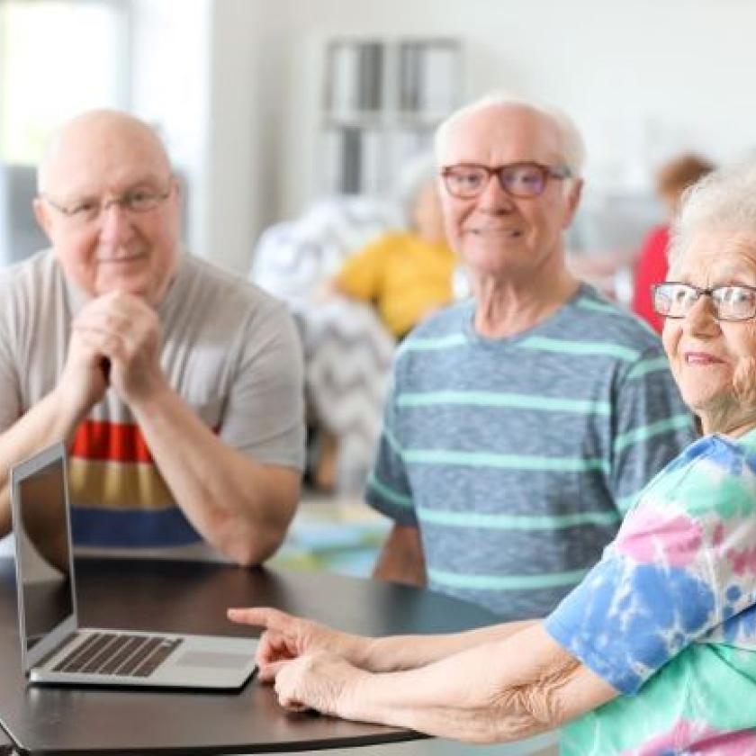 Three seniors socialise together while viewing a laptop